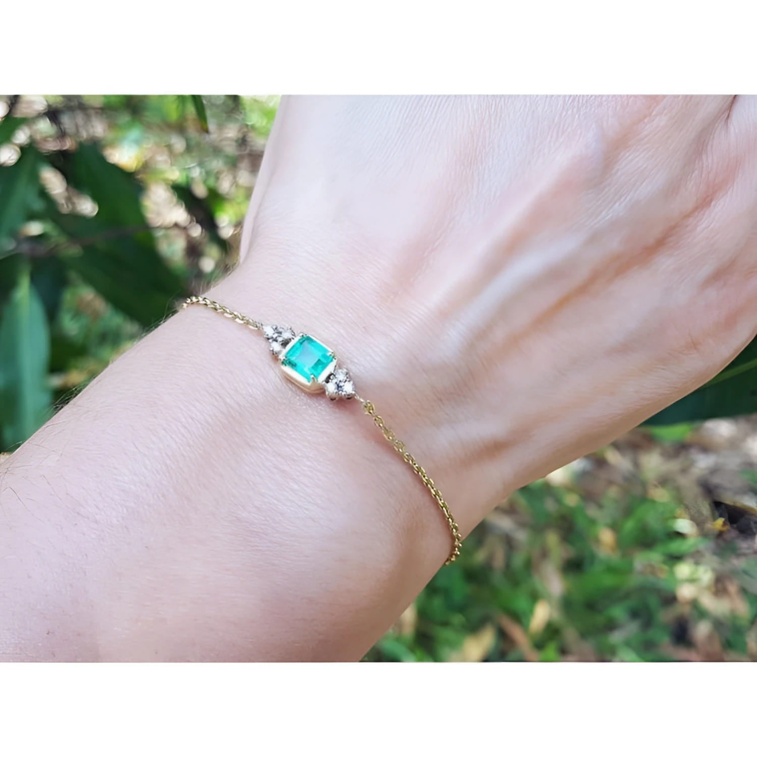 14k yellow gold emerald bracelet with a rectangular green emerald and six small diamonds on a woman's wrist.