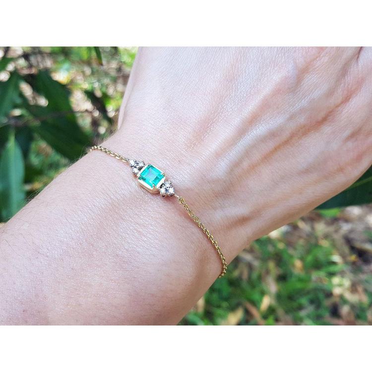 14k yellow gold emerald bracelet with a rectangular green emerald and six small diamonds on a woman's wrist.