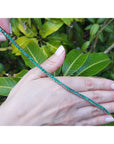 Emerald tennis bracelet held by a hand with green leaves in the background.