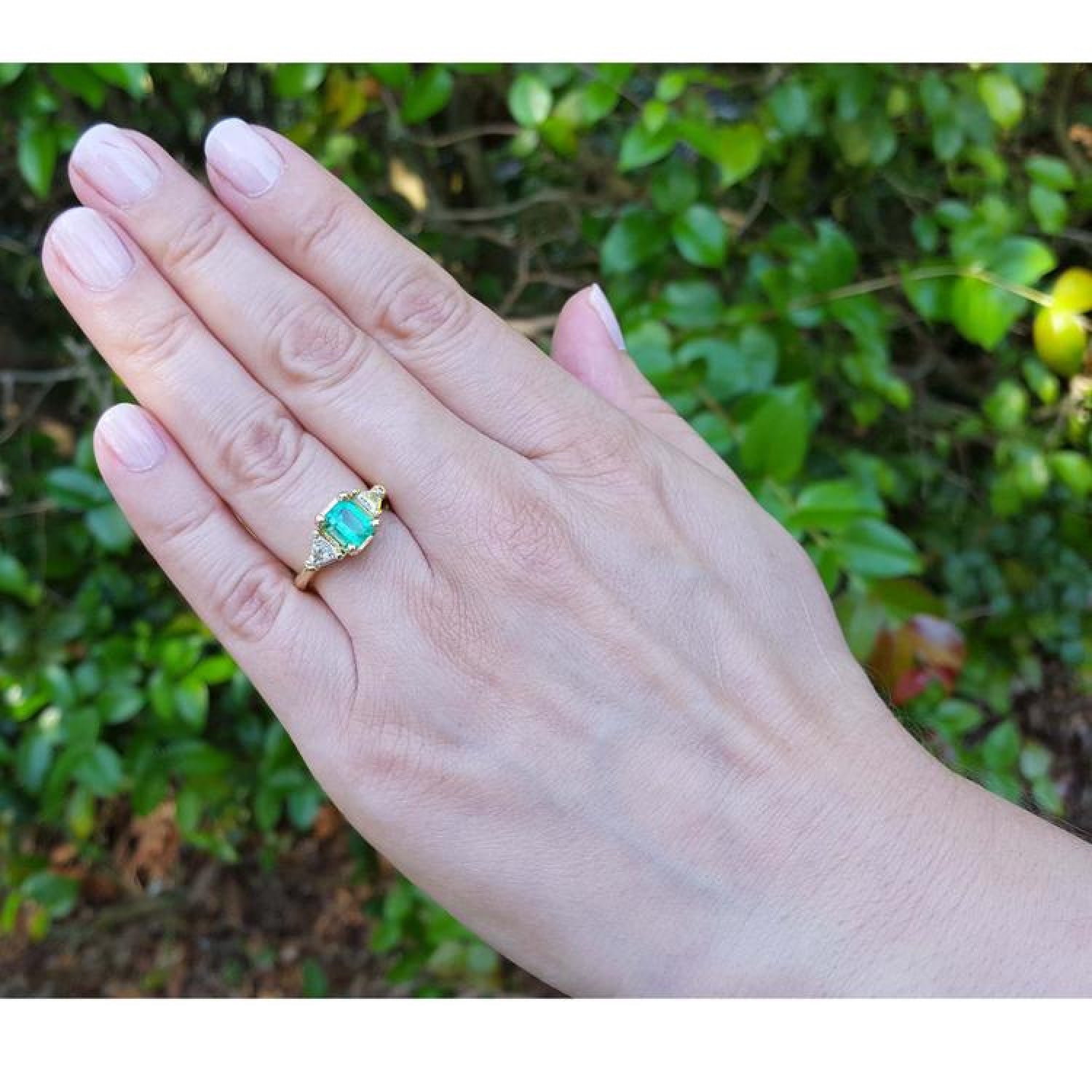 1.27 ct. natural Colombian emerald three-stone ring with trillion diamonds in 18K yellow gold on a hand.