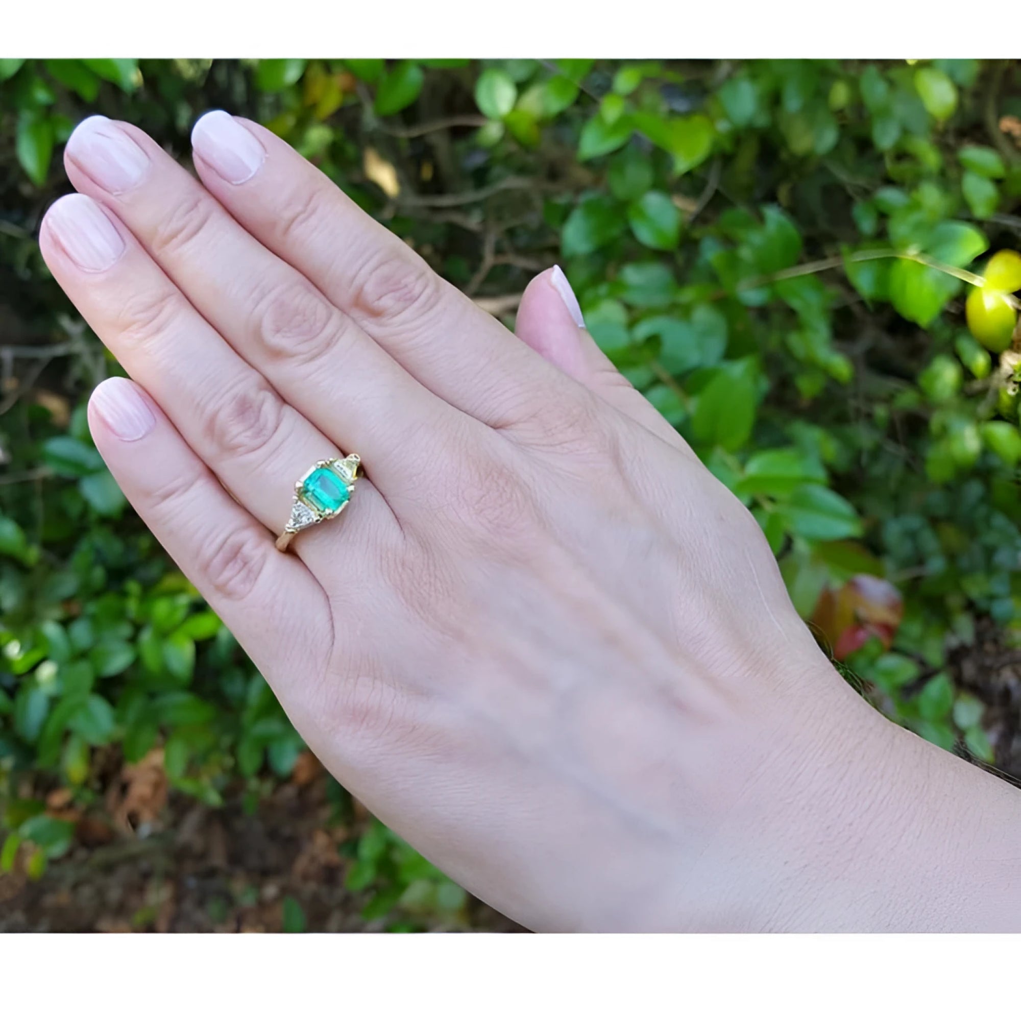 1.27 ct. natural Colombian emerald three-stone ring with trillion diamonds in 18K yellow gold on a hand.