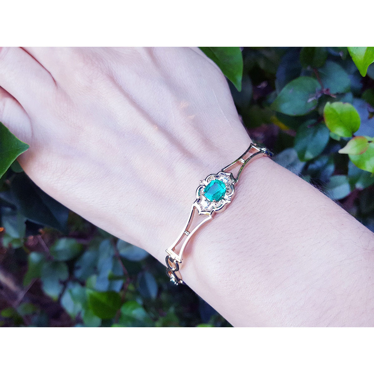 Bracelet with a genuine emerald on a wrist against a leafy background.
