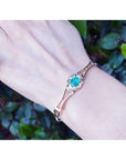 Bracelet with a genuine emerald on a wrist against a leafy background.