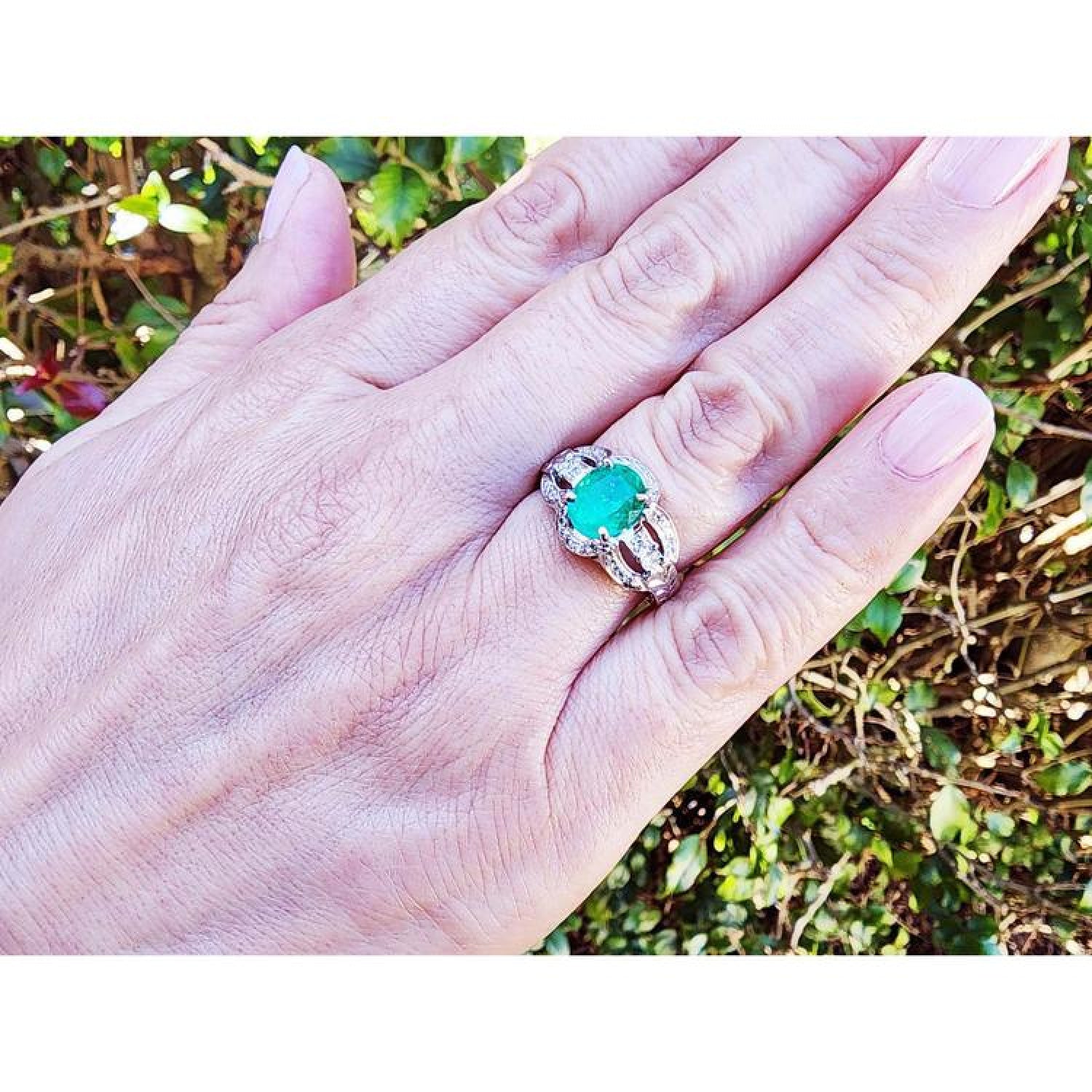 Natural oval emerald ring in 18K white gold with a decorative bridal-style band on a hand.