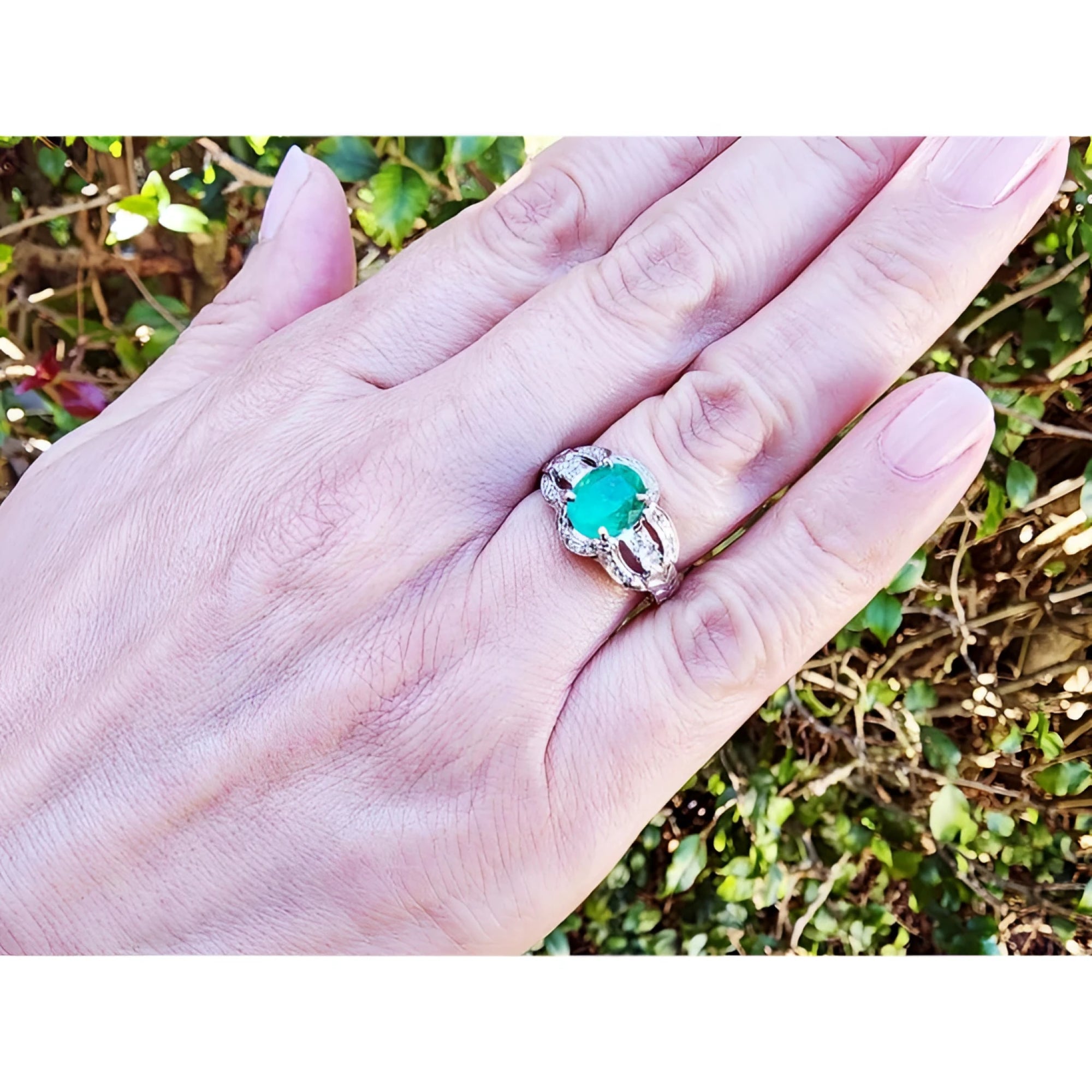 Natural oval emerald ring in 18K white gold with a decorative bridal-style band on a hand.