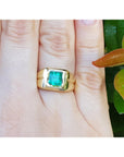 Gold ring with a square natural colombian emerald on a hand, with leaves in the background