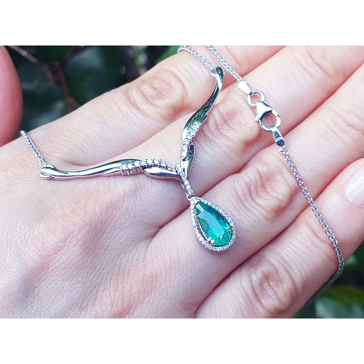 14k white gold necklace with a natural emerald teardrop pendant held in hand against a blurred natural background