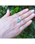 Hand displaying a natural emerald necklace with white gold chain against a green leafy background