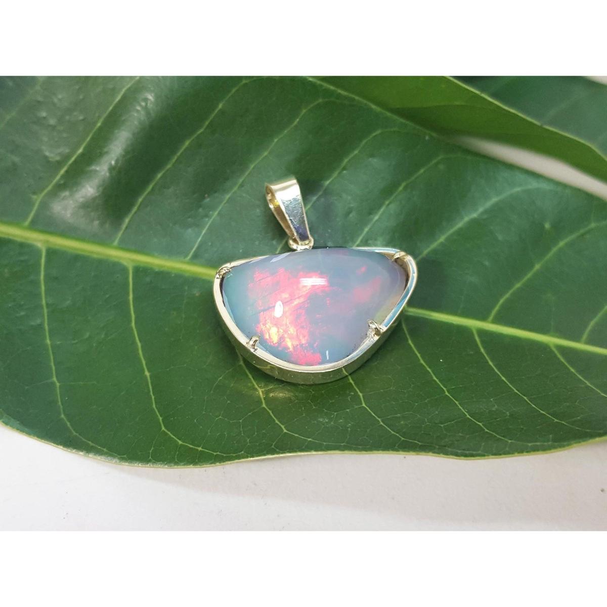 Natural Ethiopian opal pendant with gold setting on a green leaf.