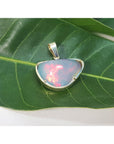 Natural Ethiopian opal pendant with gold setting on a green leaf.