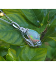 Opal pendant silver necklace on a leaf with a green leafy background.