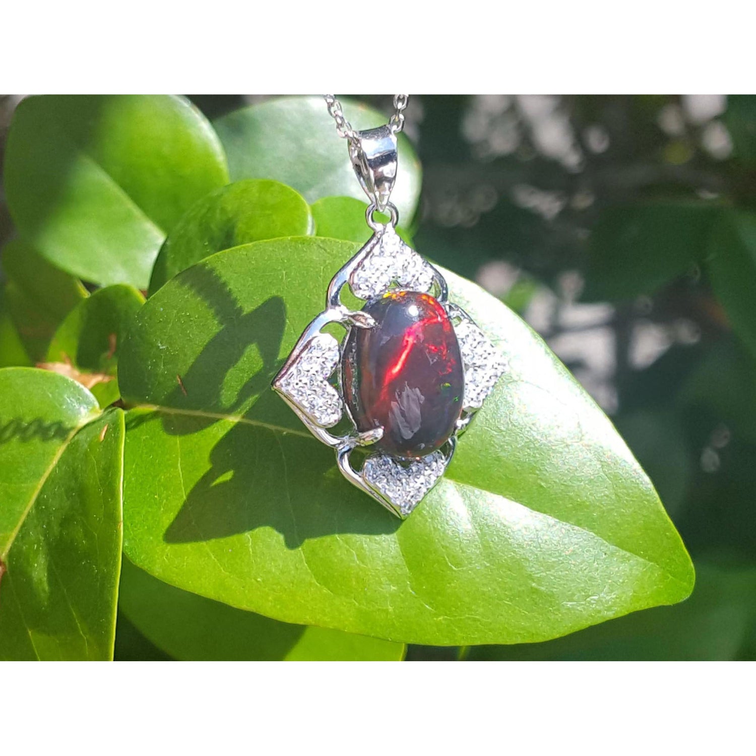 Opal pendant on a silver chain with a green leaf background.