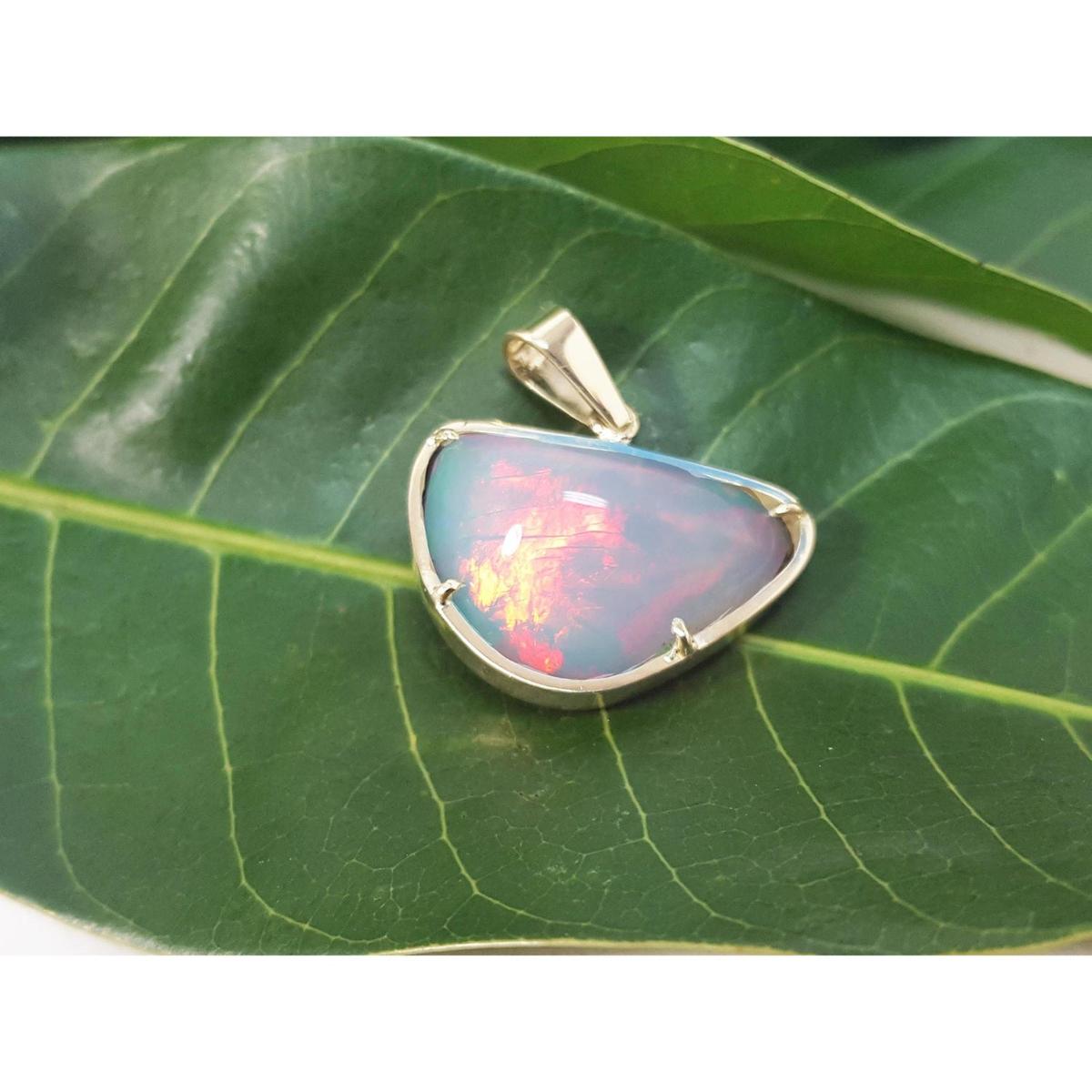 Ethiopian opal gold pendant with prong setting on a green leaf.