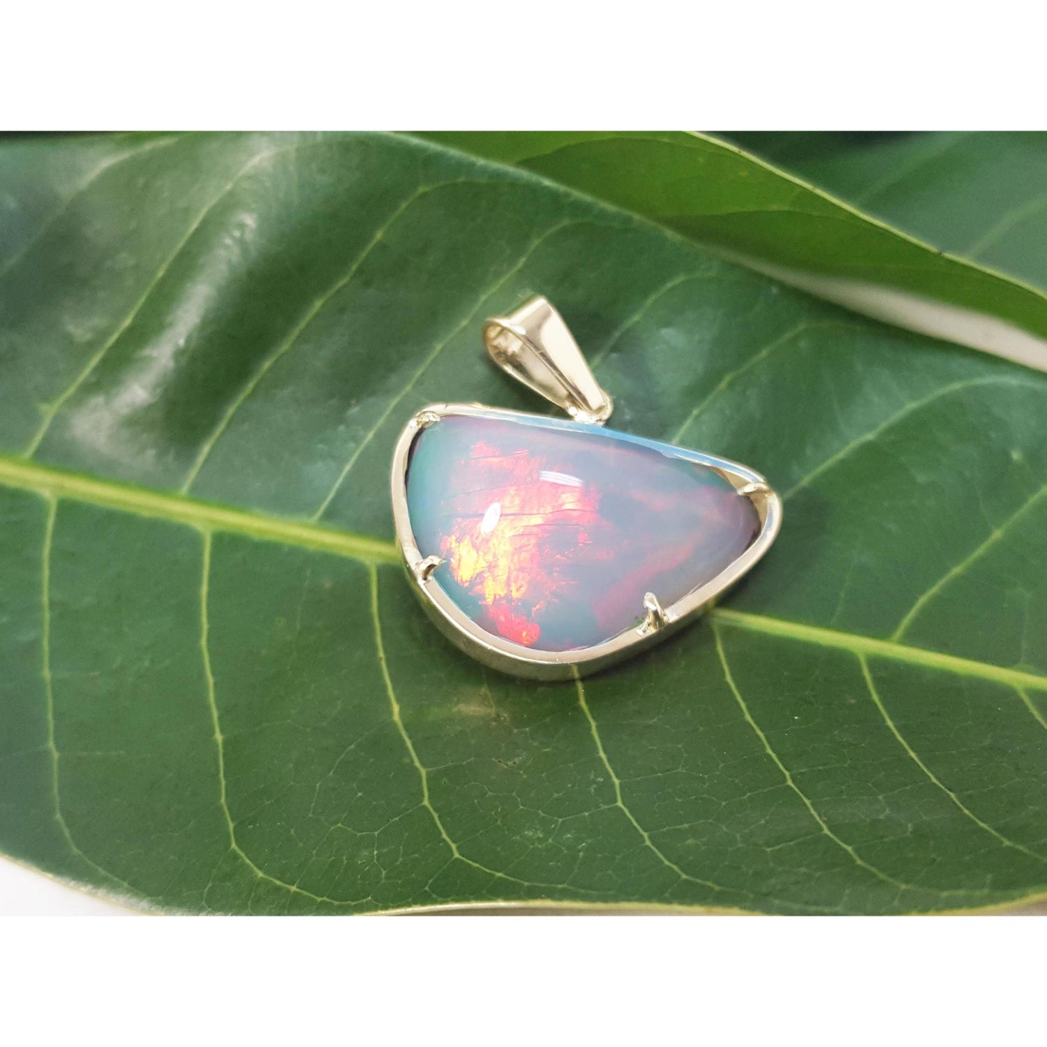 Ethiopian opal gold pendant with prong setting on a green leaf.