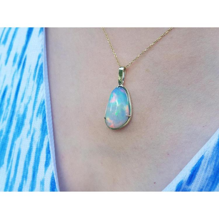 Ethiopian opal pendant with rainbow flashes in 14K yellow gold, worn on a blue and white patterned top.
