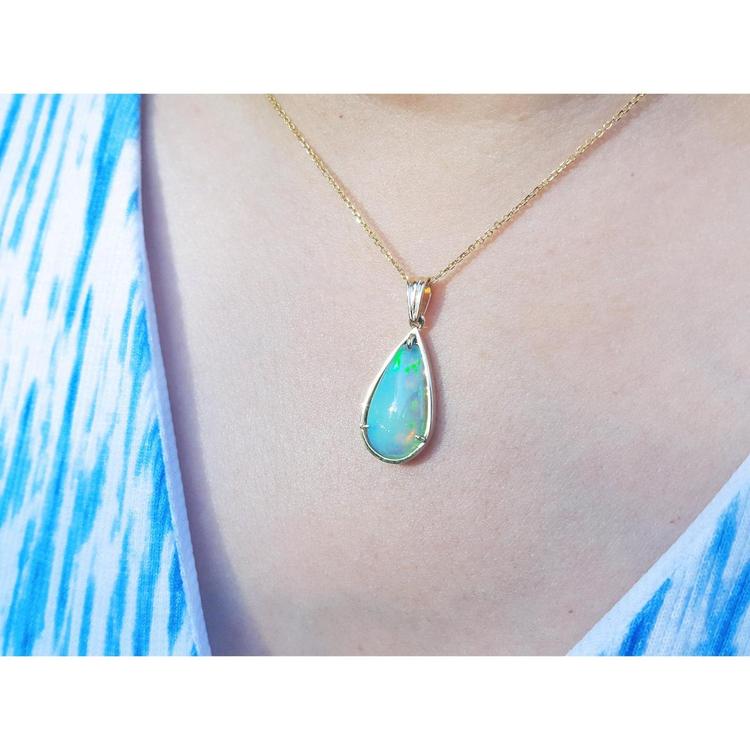 Pear-shaped Ethiopian opal pendant with blue-violet play-of-color in 14K yellow gold on a woman's neck.