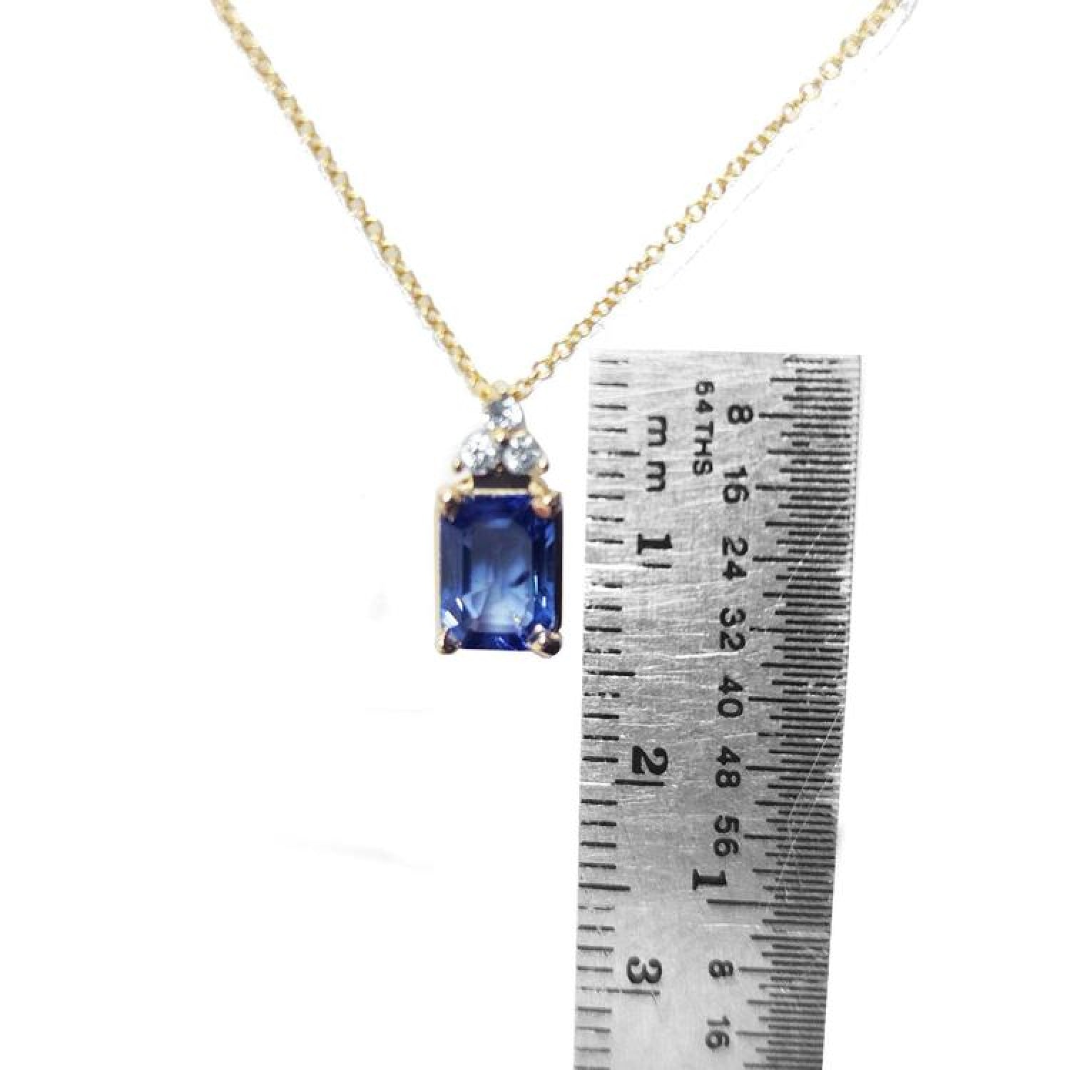 14k gold necklace with an emerald-cut blue sapphire pendant and three diamonds, next to a ruler.
