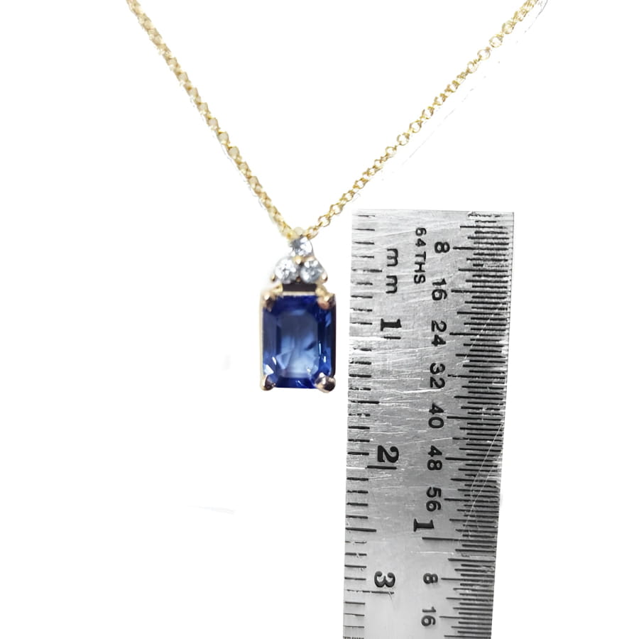 14k gold necklace with an emerald-cut blue sapphire pendant and three diamonds, next to a ruler.
