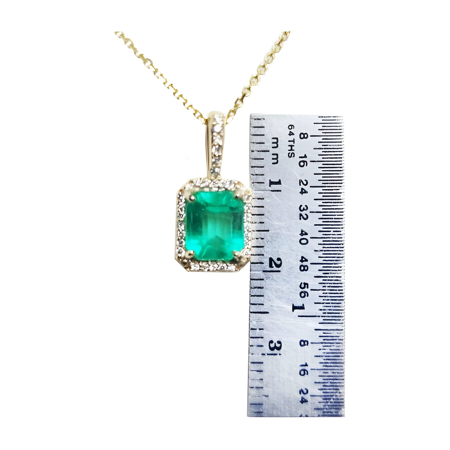 Emerald-cut Colombian emerald pendant with diamond halo on a gold chain, next to a ruler.