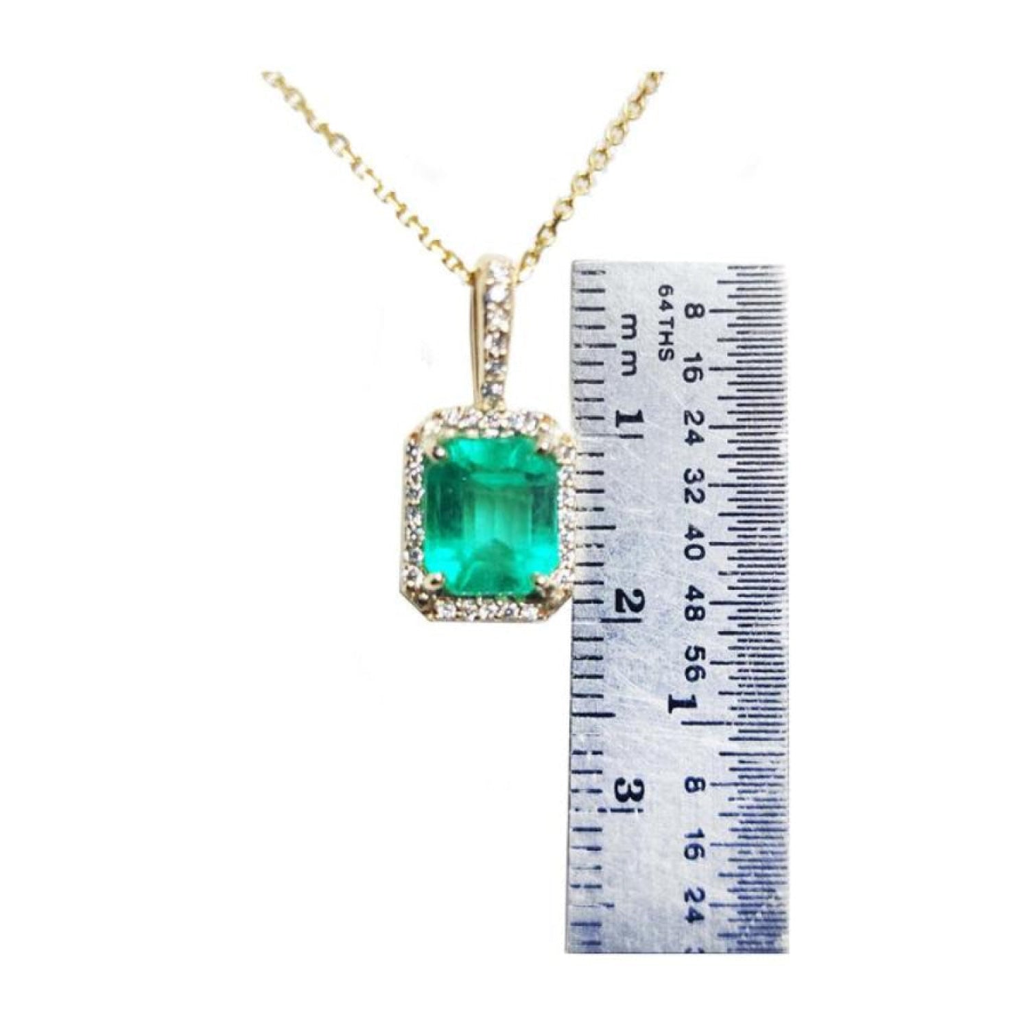 Emerald-cut Colombian emerald pendant with diamond halo on a gold chain, next to a ruler.