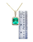 Emerald-cut Colombian emerald pendant with diamond halo on a gold chain, next to a ruler.