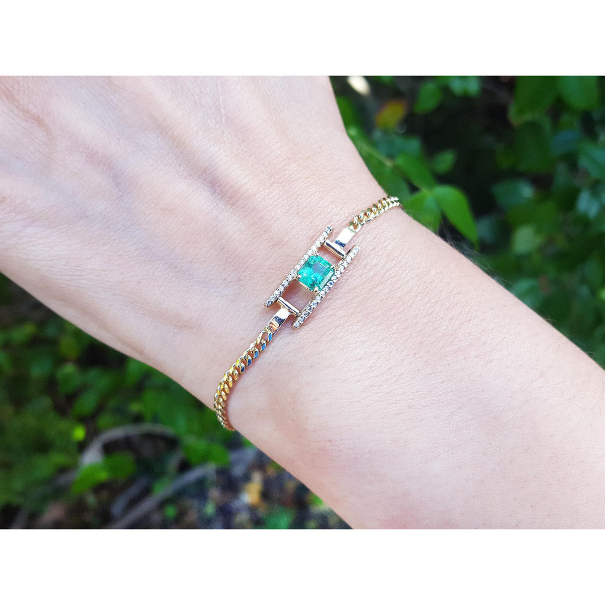 Bracelet with a colombian emerald on a wrist against a blurred green background.