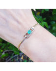 Bracelet with a colombian emerald on a wrist against a blurred green background.