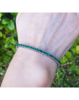 A round cut genuine colombian emerald tennis bracelet on a wrist with a blurred green leafy background