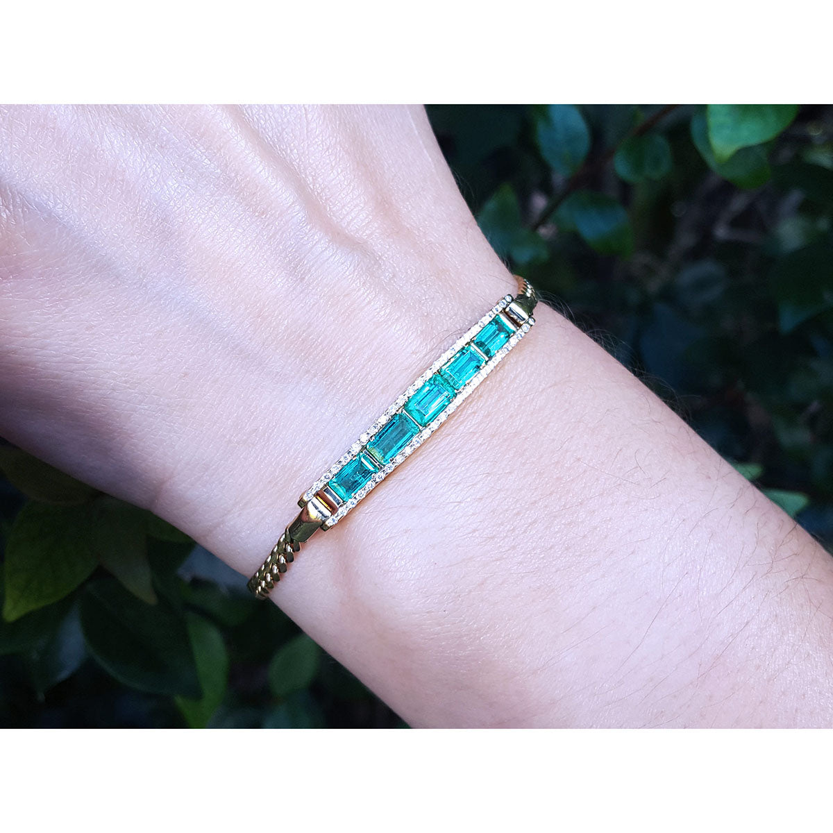 Gold bracelet with natural colombian emeralds on a wrist against a blurred natural background.
