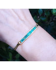 Gold bracelet with natural colombian emeralds on a wrist against a blurred natural background.