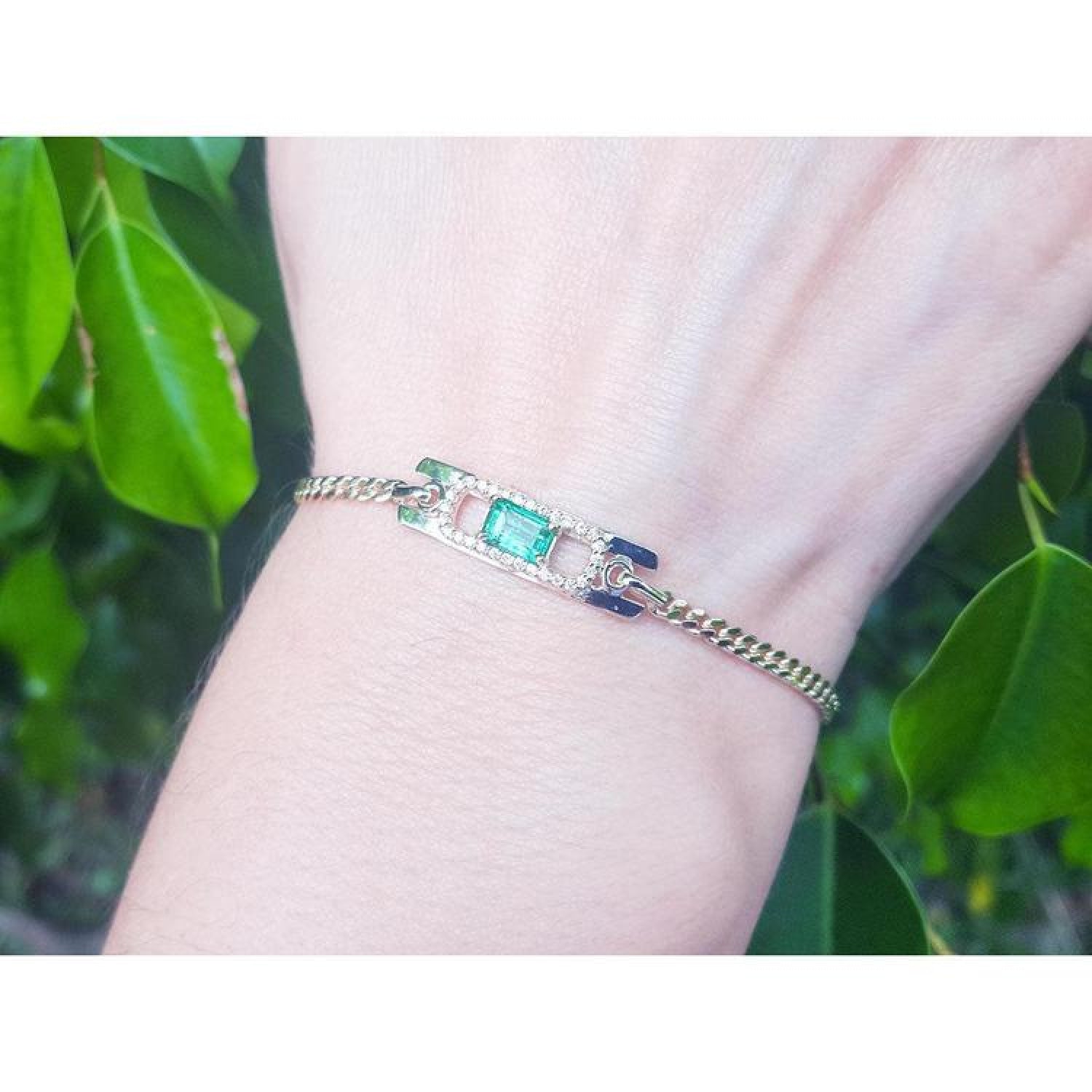 14K yellow gold bracelet with a rectangular Colombian emerald haloed by diamonds on a woman's wrist.