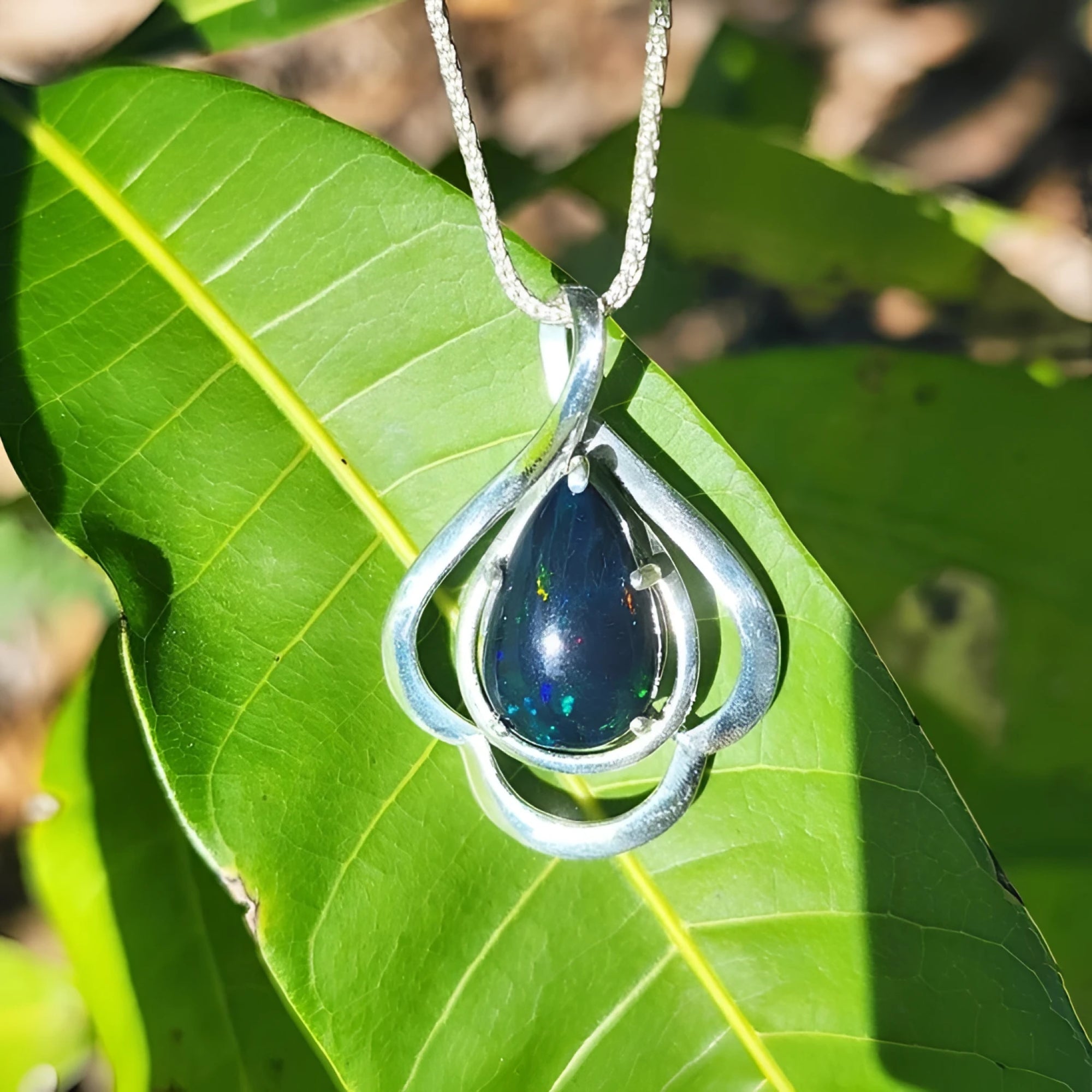 Teardrop 4.30 ct Ethiopian black opal pendant in sterling silver with multicolor flashes on a green leaf.