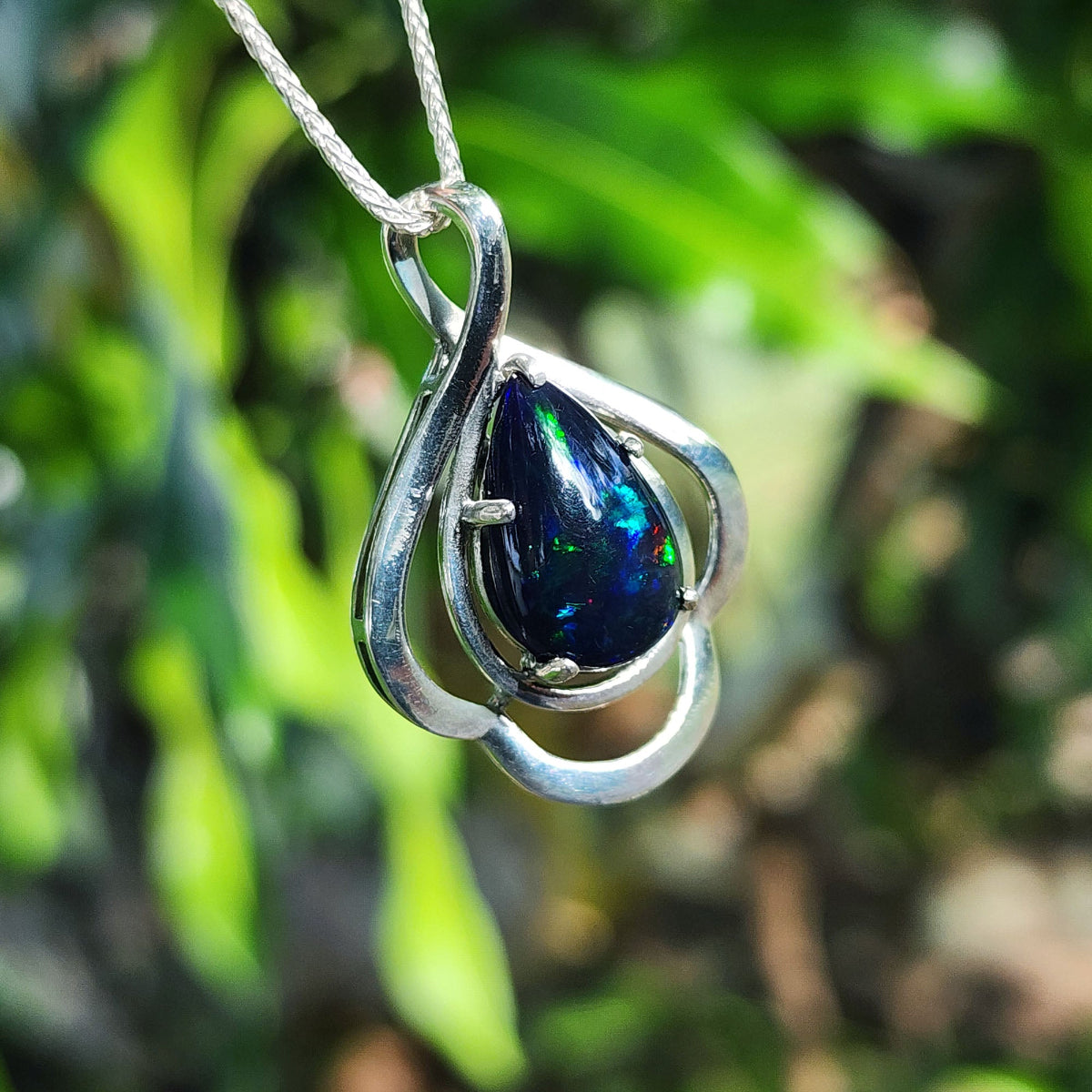 Silver pendant with a blue Ethiopian black opal against a green leafy background