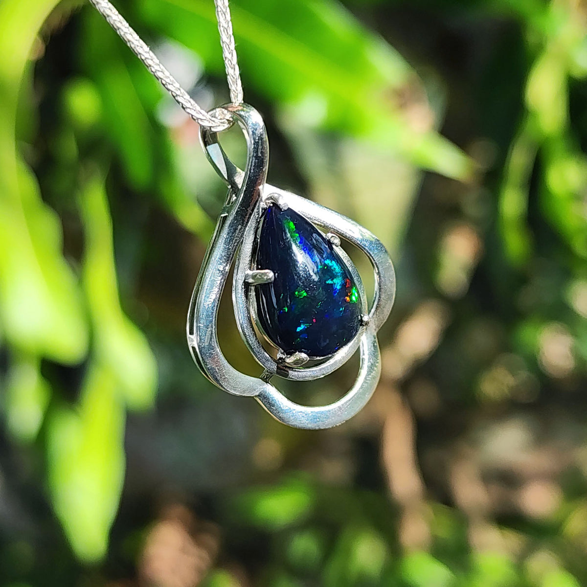 Silver pendant with a dark Welo opal teardrop against a blurred green background