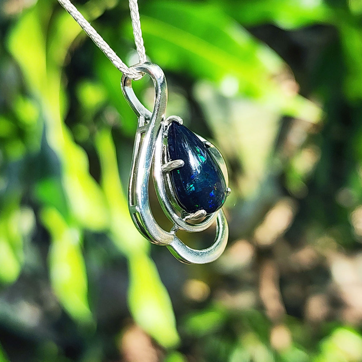 Silver pendant with a blue teardrop black opal against a blurred green background
