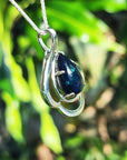 Silver pendant with a blue teardrop black opal against a blurred green background