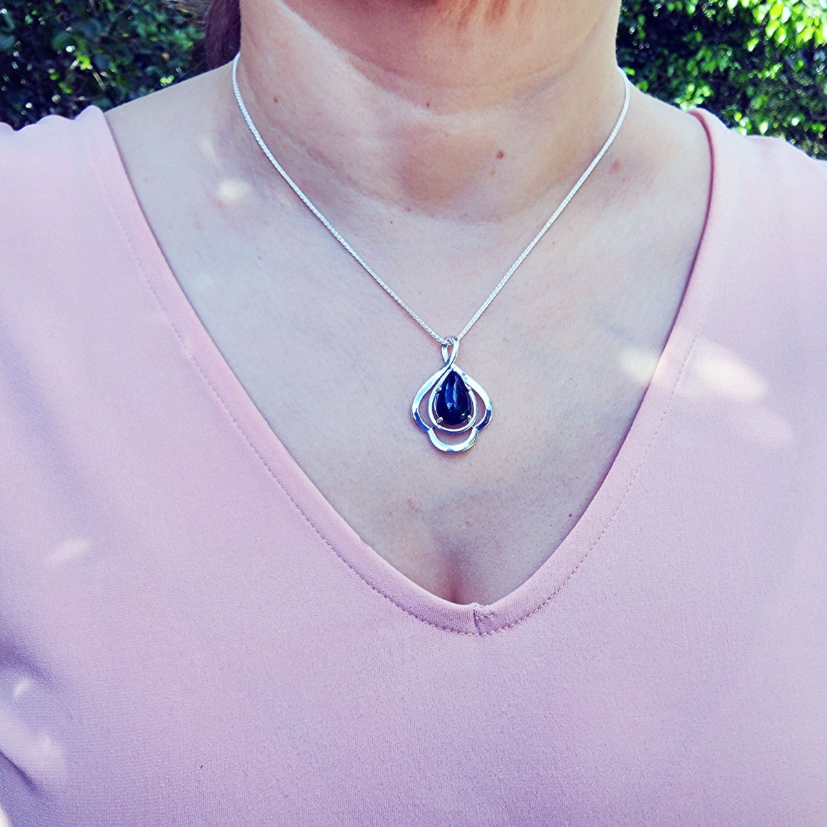 Person wearing a silver necklace with a teardrop black opal pendant outdoors