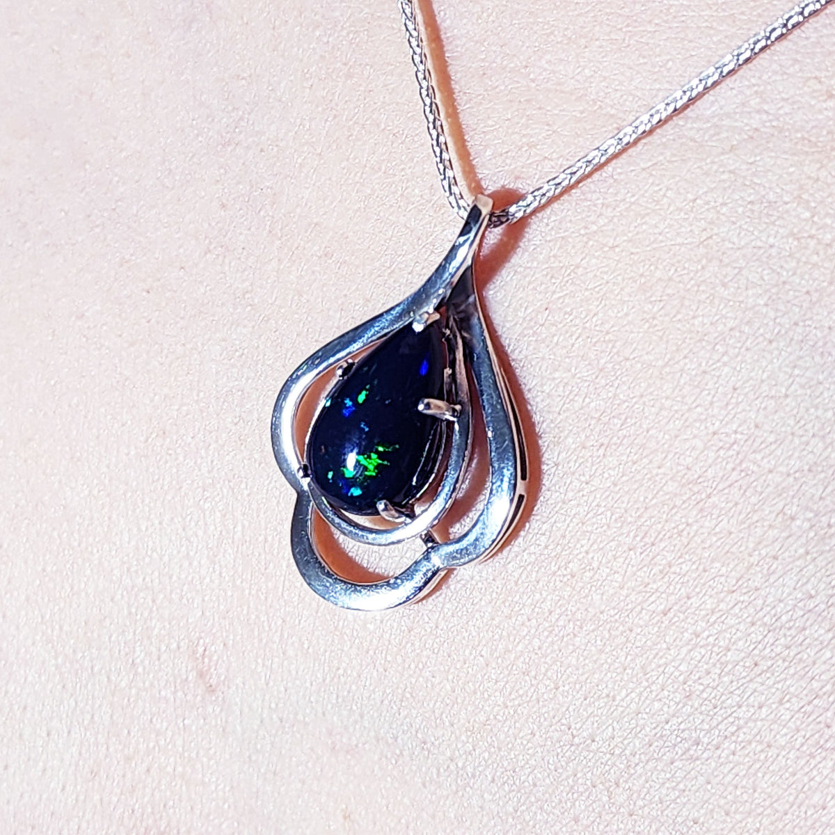 Silver pendant with a teardrop dark black opal on a light pink background