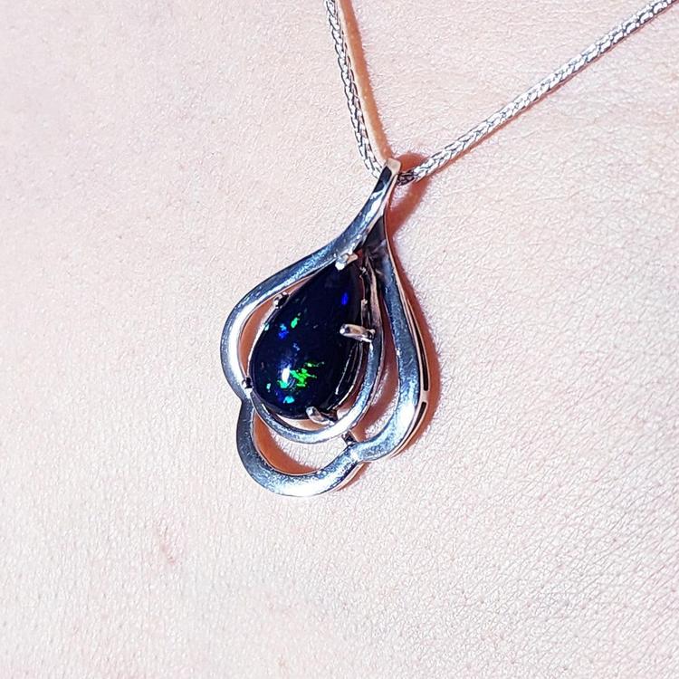 Silver pendant with a teardrop dark black opal on a light pink background