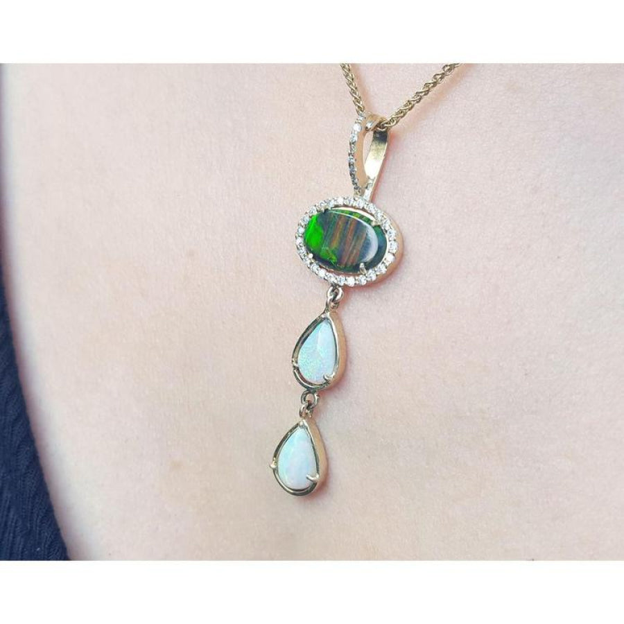 Black and white Australian opal pendant with an oval black opal, surrounded by diamonds, and two pear-shaped white opals, set in 14K yellow gold.