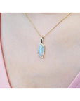 Gold necklace with a natural opal pendant on a person's neck wearing a pink top.