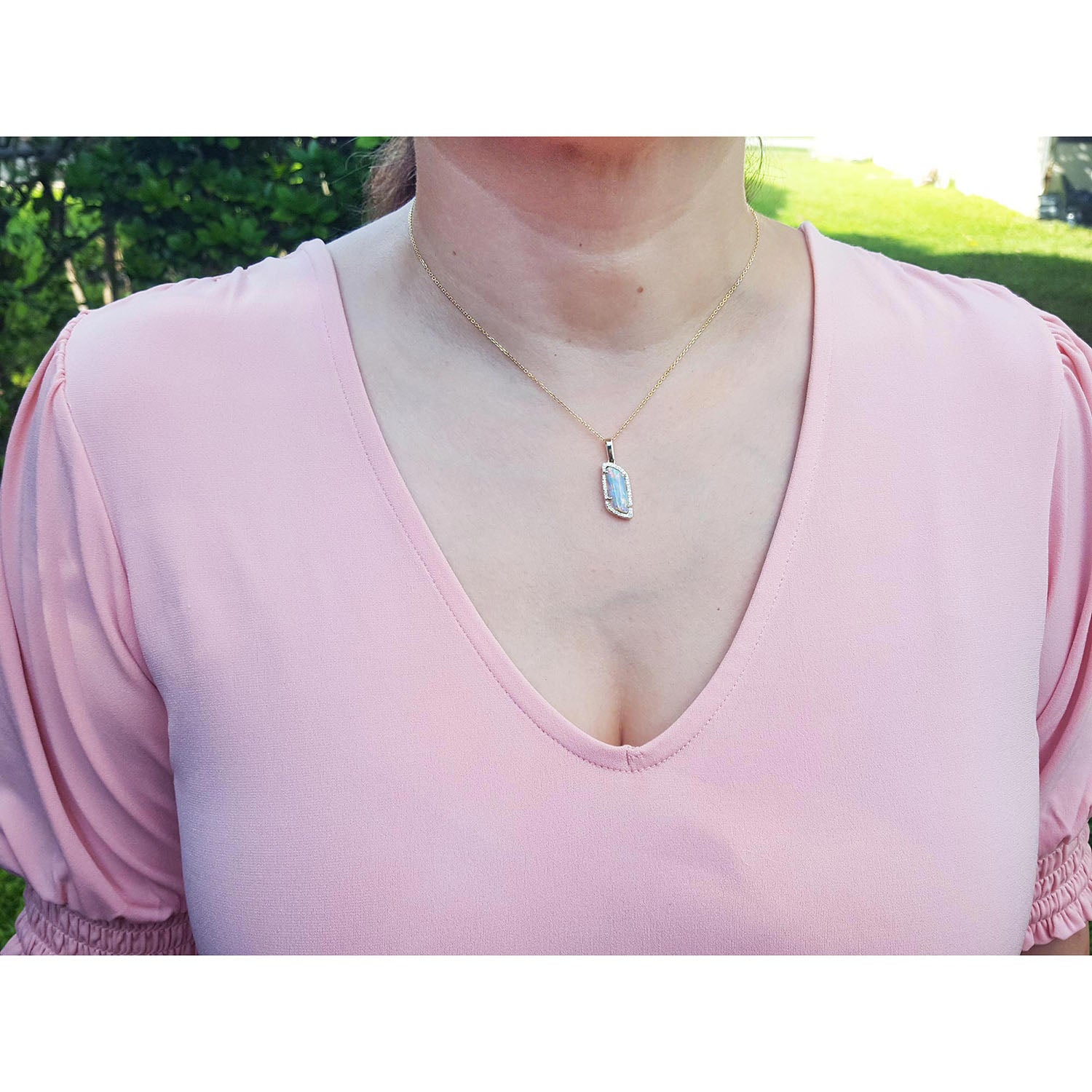 Person wearing a pink top with a necklace featuring a natural opal pendant outdoors.