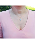 Person wearing a pink top with a necklace featuring a natural opal pendant outdoors.