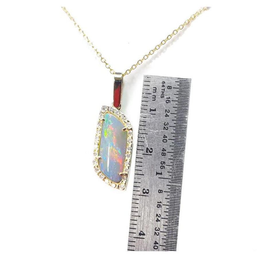 14K yellow gold pendant necklace with a colorful opal and diamond halo, next to a ruler.