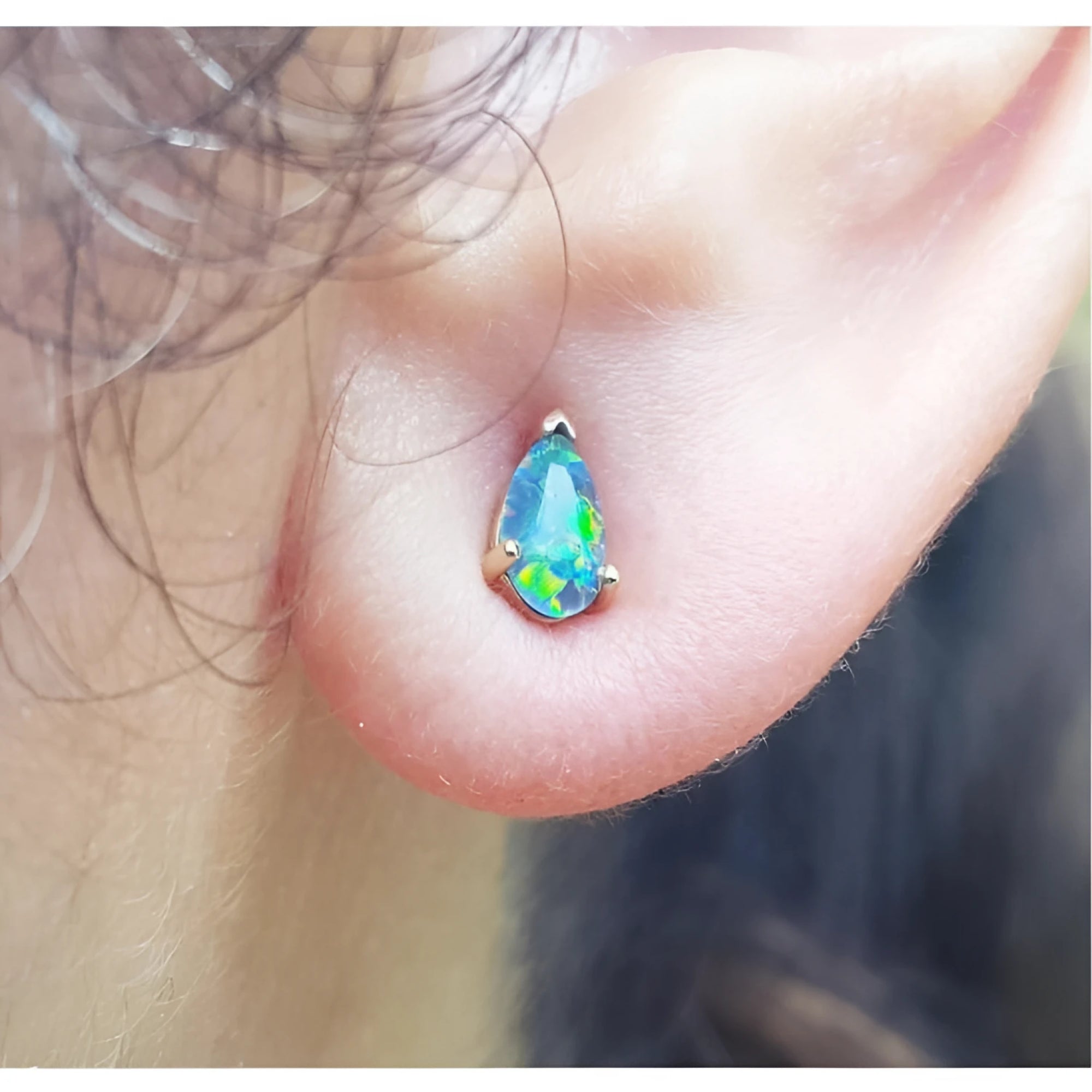 Pear-shaped Australian opal doublet stud earring with red and blue play of colors, set in 14K yellow gold.