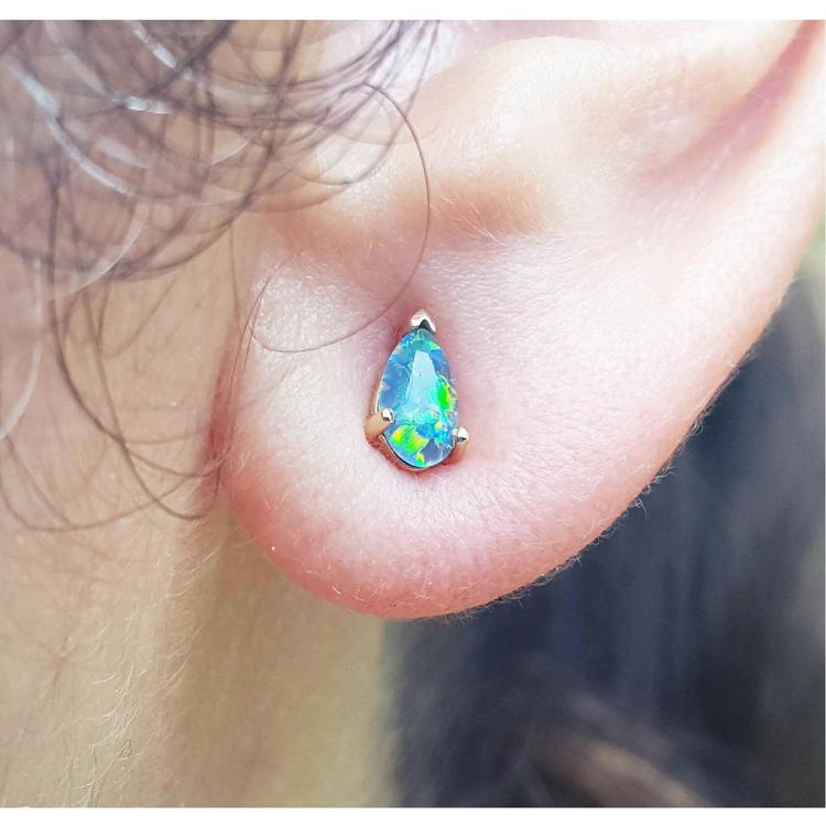 Close-up of a person wearing a teardrop-shaped opal earring.