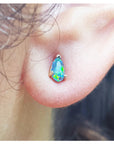 Close-up of a person wearing a teardrop-shaped opal earring.
