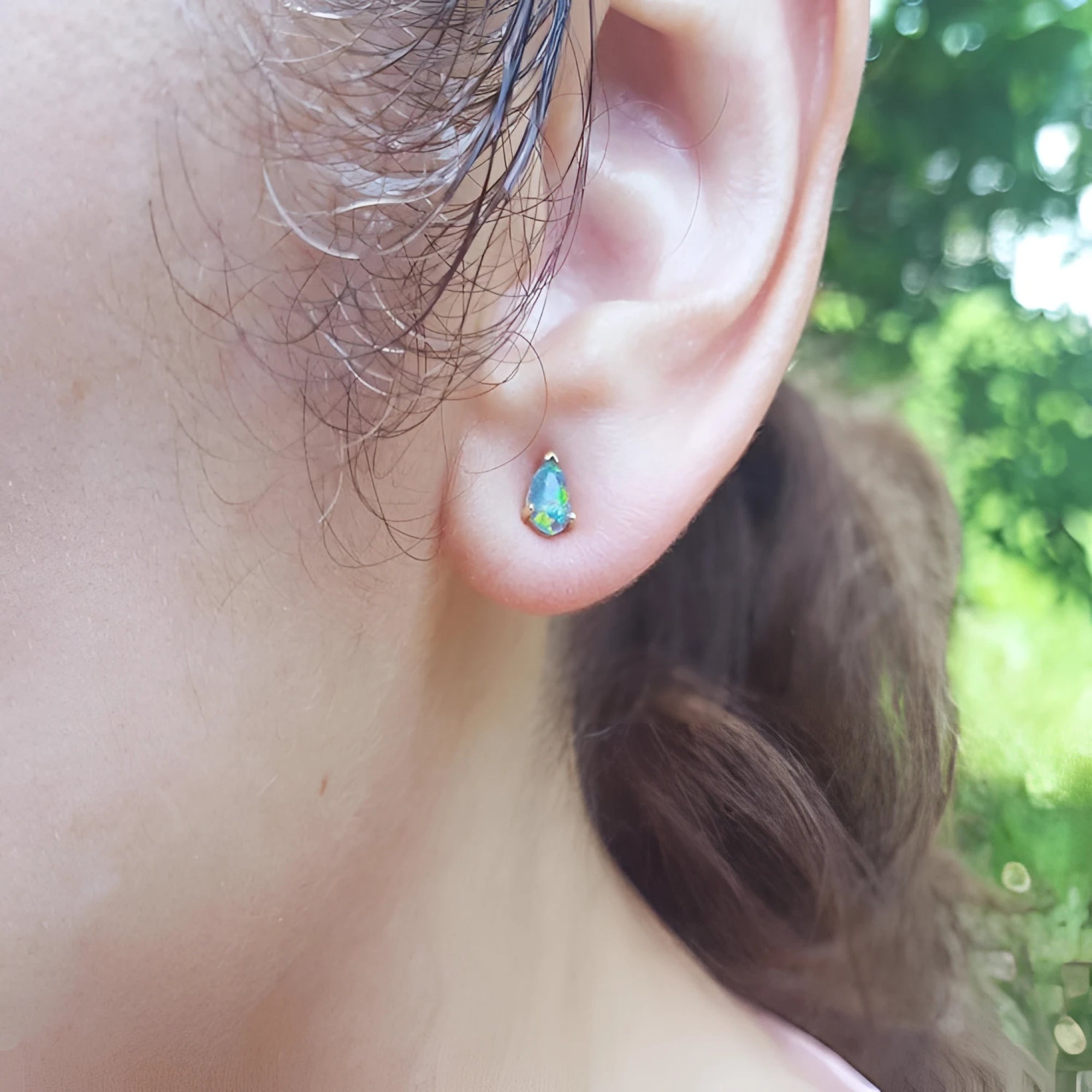 Pear-shaped opal doublet stud earring with red and blue play of colors, set in 14K yellow gold on an ear.