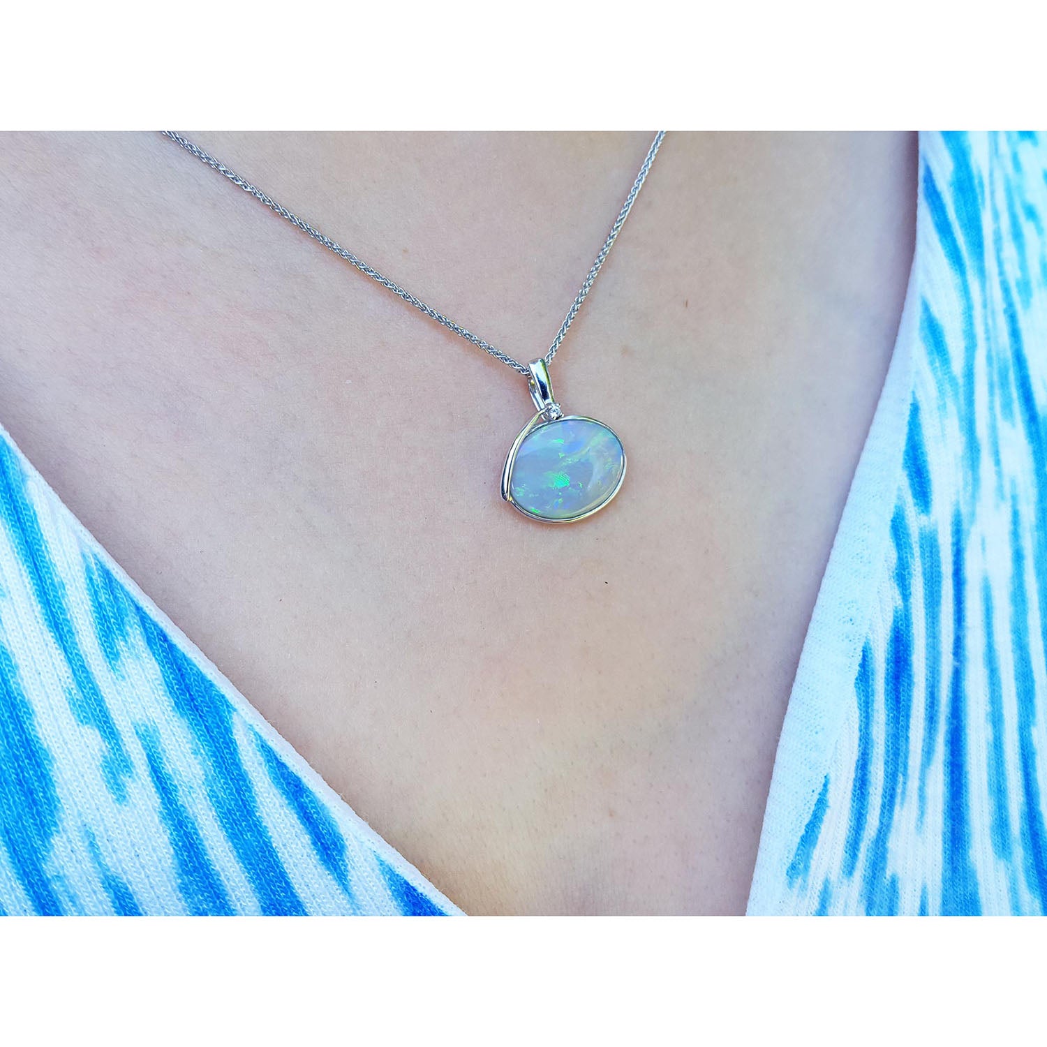 Necklace with an opal pendant worn by a person in a blue and white patterned top.