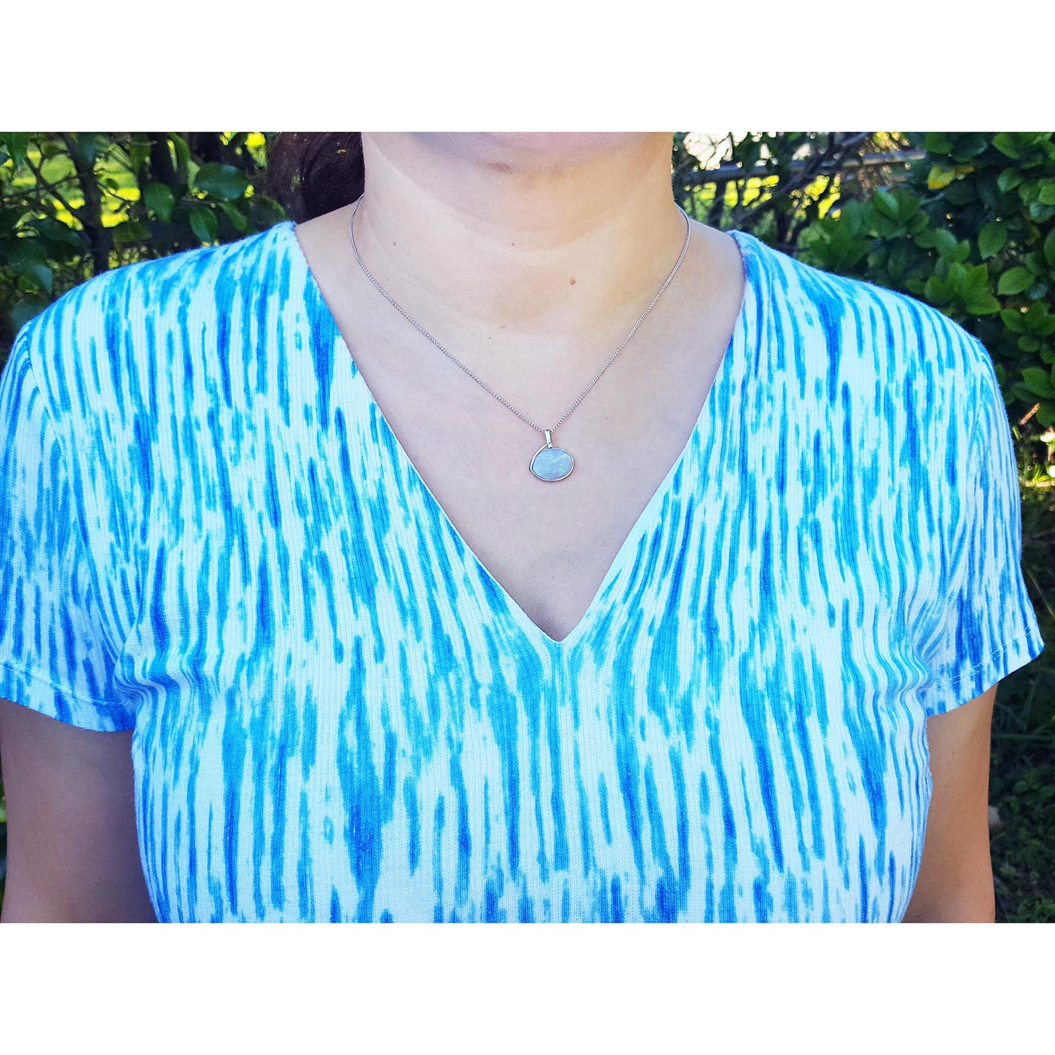 Person wearing a blue and white patterned top with a opal necklace outdoors.